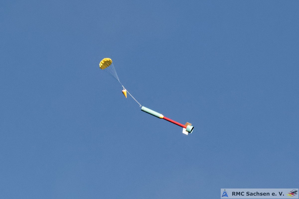 Eine Modellrakete kehrt an einem gelben Fallschirm zur Erde zurück